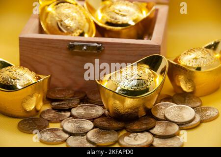 Lingotti e monete d'oro cinesi in cassa del tesoro su sfondo giallo. Concetto di ricchezza. Foto Stock