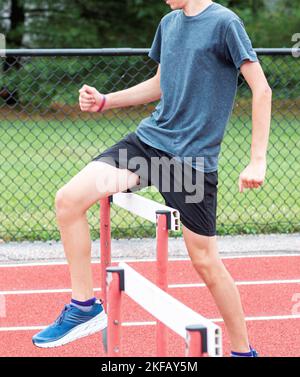 Un corridore della pista della High School che cammina sopra gli ostacoli della pista durante la pratica. Foto Stock