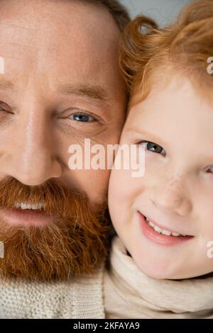 Vista ritagliata dell'uomo sorridente e del figlio dai capelli rossi che guarda la telecamera isolata sul grigio Foto Stock