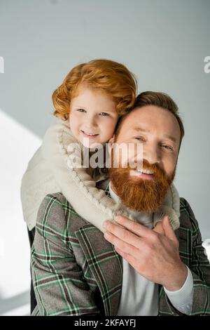 Ragazzo rosso in maglia jumper abbracciare papà bearded su sfondo grigio Foto Stock