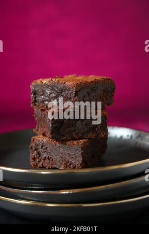 Una pila di brownie al cioccolato cotte in casa su uno sfondo rosa intenso, ideale per San Valentino Foto Stock