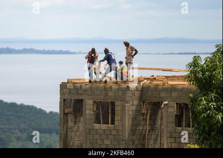 Isola di Bugala, Uganda - 30 maggio 2022: Operai edili che costruisce una casa, in piedi sul tetto, giorno di sole in maggio Foto Stock