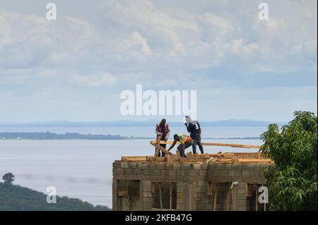 Isola di Bugala, Uganda - 30 maggio 2022: Operai edili che costruisce una casa, in piedi sul tetto, giorno di sole in maggio Foto Stock
