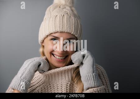ritratto di donna sorridente in caldo abbigliamento invernale su sfondo grigio. vestiti di lana a maglia Foto Stock