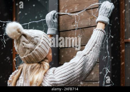 decorazioni natalizie. donna installare luci a corda elettrica sulla facciata esterna della casa Foto Stock