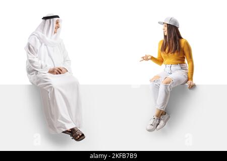 Giovane donna seduta e che ha una conversazione con un arabo in un vestiario etnico isolato su sfondo bianco Foto Stock