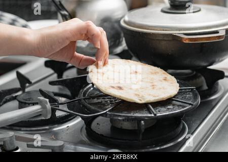 vista dettagliata, dalla mano di una ragazza che griglia un'arepa sulla griglia, girandola in modo che non bruci Foto Stock