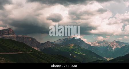 Un paesaggio panoramico con lussureggianti prati verdi e montagne dolomitiche sotto il cielo nuvoloso e blu Foto Stock
