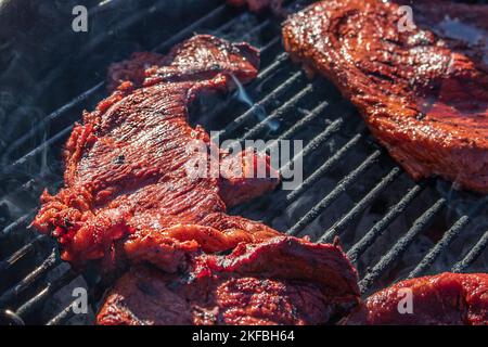 Deliziose bistecche sottili marinate grigliate su un fornello all'aperto con bolle di grasso e vapore - primo piano e focus selettivo Foto Stock