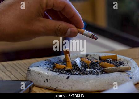 giovane uomo che fuma su un tavolo di legno, posacenere con diversi sigari usati, messico Foto Stock
