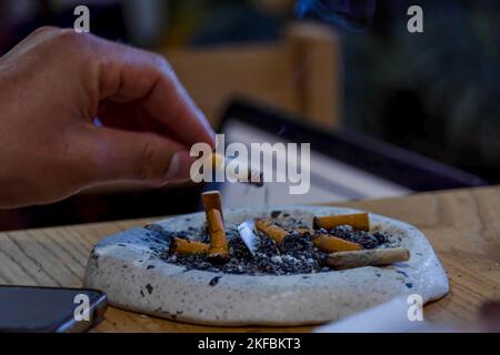 giovane uomo che fuma su un tavolo di legno, posacenere con diversi sigari usati, messico Foto Stock