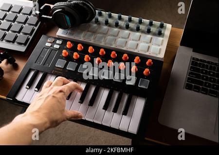 Cuffie da studio su una tastiera midi e la mano di un musicista sui tasti. Attrezzatura professionale per studio di registrazione, studio di musica. Attività professionali Foto Stock