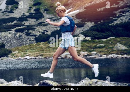 Bella donna bionda sta correndo in montagna su rocce e pietre. Foto Stock