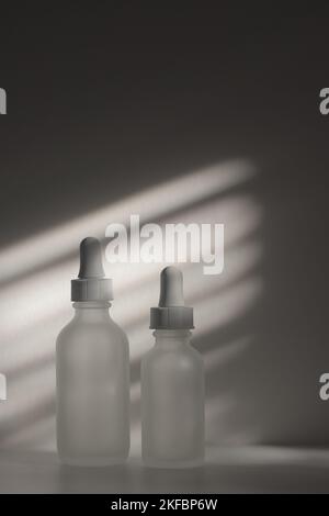 Due fiale contagocce in vetro semitrasparente vuote. Bottiglie di diverse dimensioni su sfondo bianco con luce naturale e appiccita. Spazio copia bellezza verticale. Foto Stock