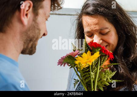 giovane donna brasiliana con gli occhi chiusi, felice e sorridente sente l'odore di un bouquet di fiori che suo marito le ha regalato per i valentini. Foto Stock
