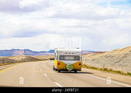 Un camper retro giallo e bianco si muove nella zona dei badlands dello Utah vicino all'Arches National Park, con lo sfondo del dessert di partenza su una strada a due corsie Foto Stock