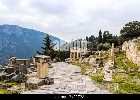 Rock passerella giù per la collina nell'antica Grecia Delphi passato colonne ioniche e parti di templi e passato un tesoro ricostruito con montagna in distanza Foto Stock