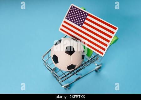 Palla di calcio con bandiera USA nel carrello della spesa su sfondo blu. Guadagni della coppa di calcio. Foto Stock