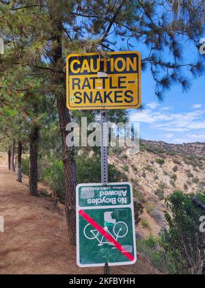 Uno scatto verticale di un segnale di attenzione che avverte circa i rastlesnakes ed un altro che vieta il ciclismo Foto Stock