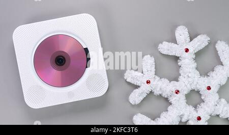 Elegante lettore CD portatile bianco con CD rosa che riproduce musica natalizia con fiocco di neve bianco su sfondo grigio. Rétro vintage di tendenza dis Foto Stock