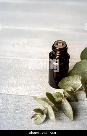Olio essenziale in una piccola fiala di vetro con rametti di eucalipto su fondo di legno. Messa a fuoco selettiva e spazio di copia per il testo. Prodotti cosmetici naturali. Foto Stock