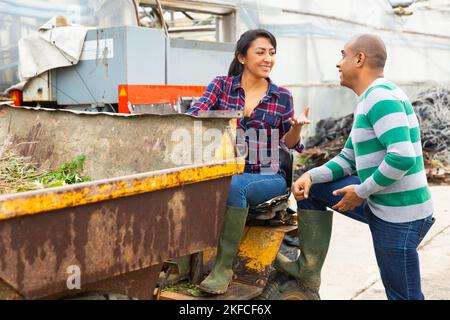 Donna contadina latino-americana che guida un camion mini dump, comunica con un collega maschio. Foto Stock