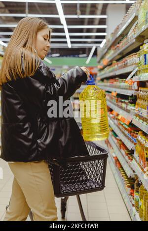 Donna che acquista oli da cucina per cibo in supermercato, mettere grande bottiglia in carrello Foto Stock