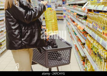 Donna che acquista oli da cucina per cibo in supermercato, mettere grande bottiglia in carrello Foto Stock