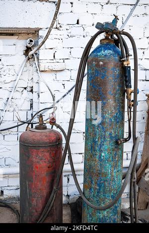 Vecchie bombole di gas per saldatura e taglio. Serbatoi di propano e ossigeno arrugginiti. Utensili per l'industria metallurgica. Cantiere abbandonato. Foto Stock