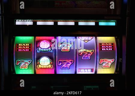 Le ruote illuminate delle slot machine attirano i giocatori con la loro grafica colorata e le sequenze lampeggianti in arcate di divertimento scarsamente illuminate. Foto Stock