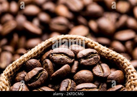 Chicchi di caffè arrostiti in un sacco di stoffa, su sfondo scuro, immagine ravvicinata, spazio per il testo Foto Stock