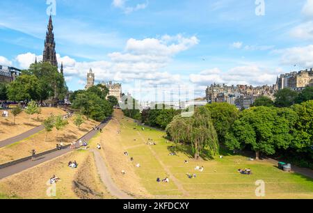 Edimburgo, Scozia, luglio 30 2022: Durante la stagione estiva del Fringe Festival, molte persone si siedono e si rilassano sull'erba baciata dal sole, vicino allo Scott Monument Foto Stock