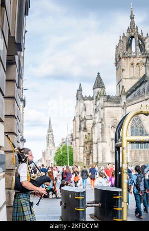 Edimburgo, Scozia-luglio 30 2022: Un giocatore scozzese di pipe in abiti tradizionali scozzesi, busks per turisti e passanti vicino, accanto alle barriere di sicurezza, durin Foto Stock