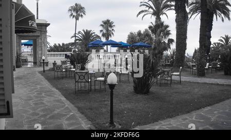 Una vista semi-colorata di tavoli e sedie vuoti nel giardino del Grand Hotel Villa de France in Marocco Foto Stock