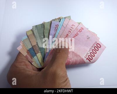 Primo piano isolato sulla mano bianca in possesso di denaro diverse banconote denominate in rupiah. Rupiah è la valuta dell'Indonesia Foto Stock