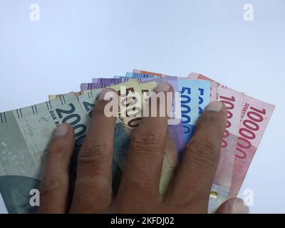 Primo piano isolato sulla mano bianca in possesso di denaro diverse banconote denominate in rupiah. Rupiah è la valuta dell'Indonesia Foto Stock