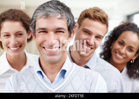 Mantenere il team positivo. Primo piano di un professionista dall'aspetto positivo con i suoi colleghi che si trovano dietro di lui. Foto Stock