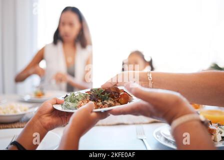 Famiglia, cibo e pranzo a un tavolo con le mani di persone che servono piatto con insalata per uno stile di vita sano in una sala da pranzo a casa. Donne sedute Foto Stock