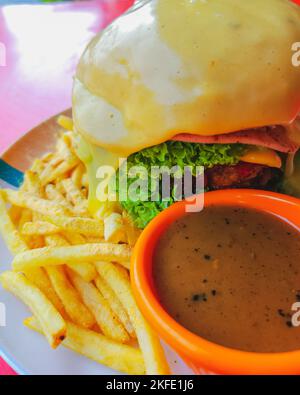 Cheeseburger di manzo con formaggio fuso servito con salsa di pepe nero e patatine fritte. Foto Stock