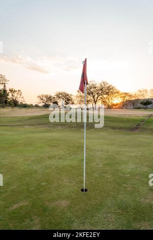Tramonto su un putting green con una bandiera nella tazza su un campo da golf a Mpumalanga, Sud Africa concetto di golf e sport Foto Stock