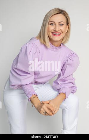 Adorabile donna adulta con il trucco di sollevamento perfetto in blusa di lavanda delicata isolato su bianco. Ritratto della donna felice di successo di affari Foto Stock