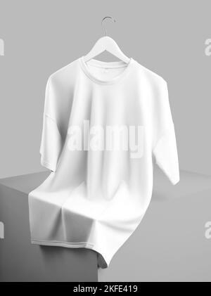 Beffa di una t-shirt bianca oversize appesa a un appendiabiti, disposta su un cubo, vista frontale, isolata sullo sfondo. Modello di abbigliamento in bianco Foto Stock