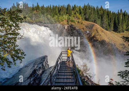 Ragazze in piedi sul ponte panoramico presso la famosa cascata Tannforsen nord della Svezia, con un arcobaleno nella nebbia e rapide cascate d'acqua. Foto Stock