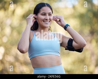 Donna, fitness e musica con un atleta indossando auricolari per la motivazione canzoni prima di un esercizio fisico in natura. Allenarsi, correre e atletica Foto Stock