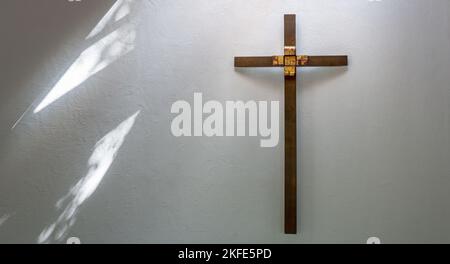 Croce cristiana in legno marrone con decorazione in oro su una parete bianca Foto Stock