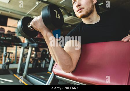 Giovane atleta maschile esegue esercizi con manubri in palestra. Allenamento di forza Foto Stock