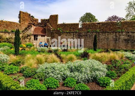 Due visitatori si riposano su una panca da giardino nel giardino murato delle rovine del Palazzo Vescovile a Wells, Somerset, Inghilterra, Regno Unito Foto Stock