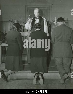 Vescovo episcopale che conferma i tenenti afroamericani Rosemary Vincent e Hallie M. Brown e un soldato non identificato, mentre si inginocchiano davanti a lui, 1939 - 1945. Foto Stock