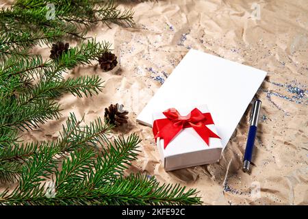 Diversi fogli bianchi di cancelleria per la scrittura su uno sfondo di Capodanno e una scatola regalo con un bel arco rosso. Felice anno nuovo e Buon Natale. Obiettivi o promesse di Capodanno con decorazioni colorate sullo sfondo di carta kraft sbriciolato con rami di albero di Natale. Angolo alto. Foto Stock