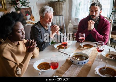 Famiglia e concetto religioso. Gruppo di persone multietniche con cibo che prega prima del pasto Foto Stock